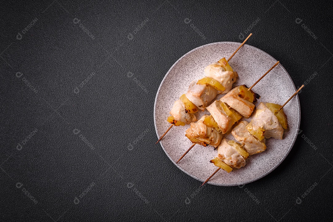 Delicioso kebab de frango ou peru com pedaços de abacaxi em espetos com sal, especiarias e ervas em um fundo escuro de concreto