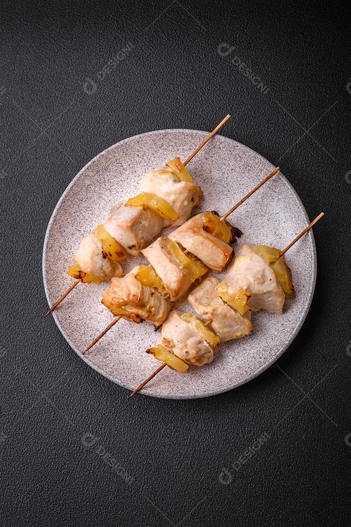 Delicioso kebab de frango ou peru com pedaços de abacaxi em espetos com sal, especiarias e ervas em um fundo escuro de concreto