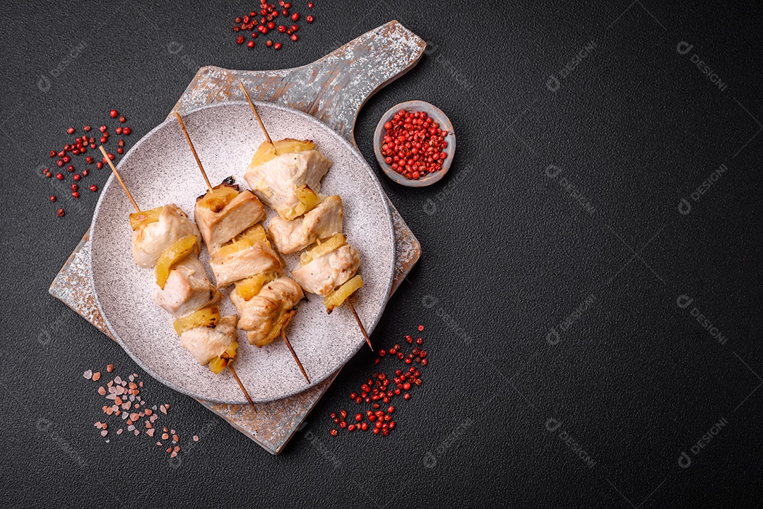 Delicioso kebab de frango ou peru com pedaços de abacaxi em espetos com sal, especiarias e ervas em um fundo escuro de concreto