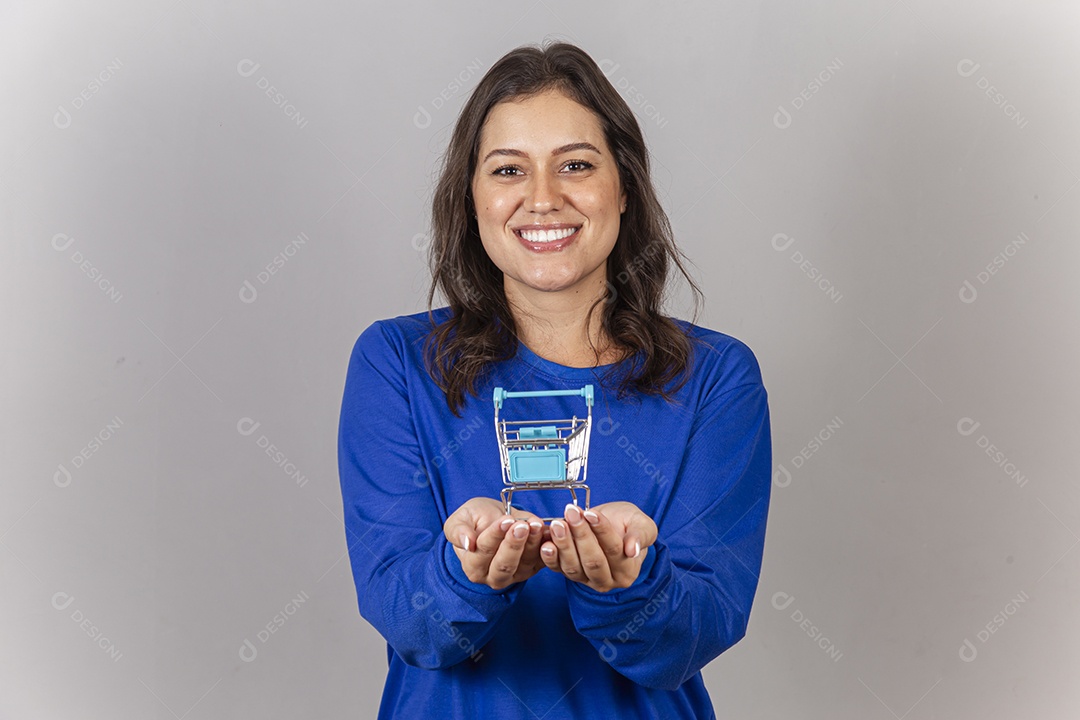 Jovem mulher sorridente com mini carrinho de supermercado nas mãos.