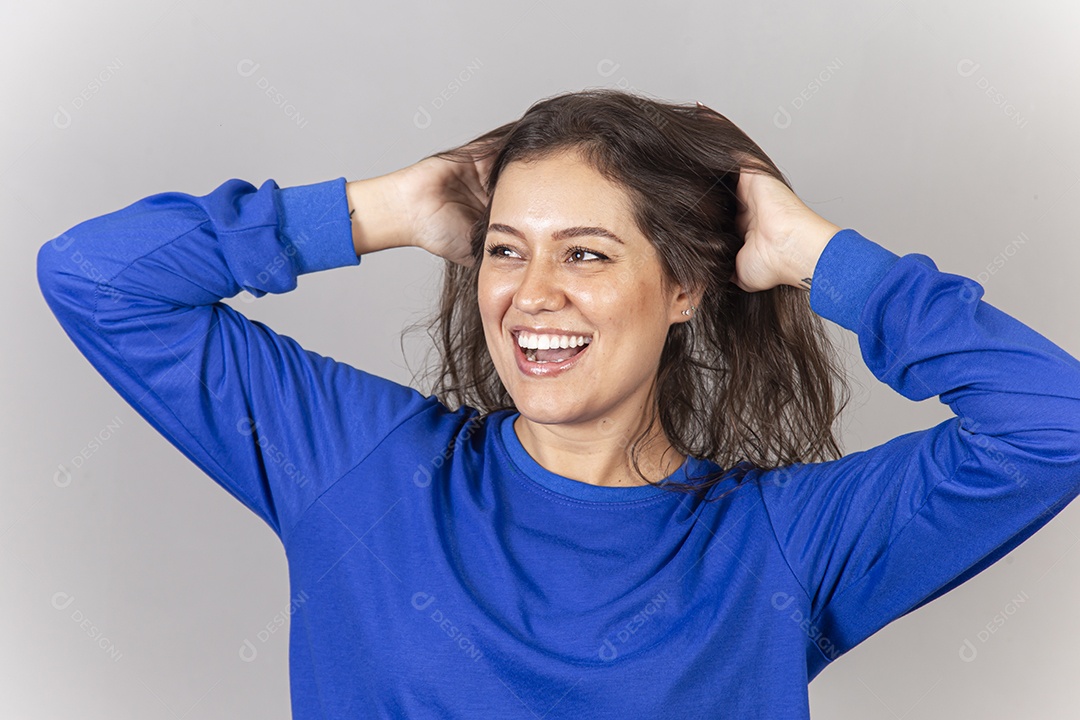 Linda jovem mulher vestida com moletom azul com as mãos entre os cabelos.