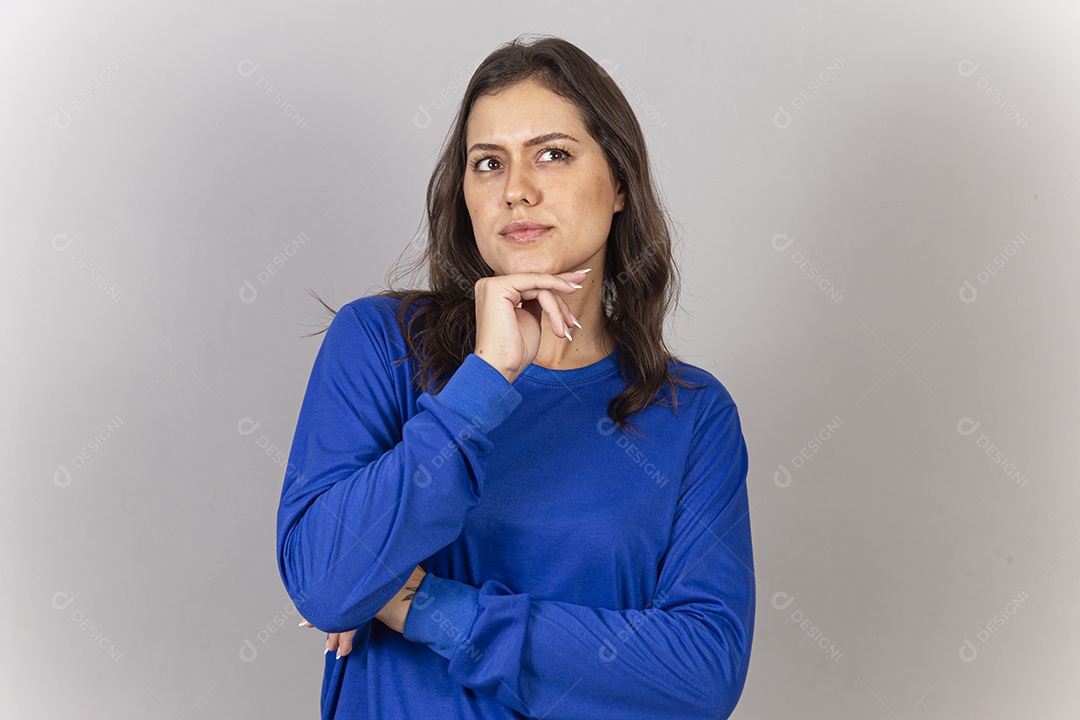 Linda jovem mulher vestida com moletom azul com a mão embaixo do queixo.