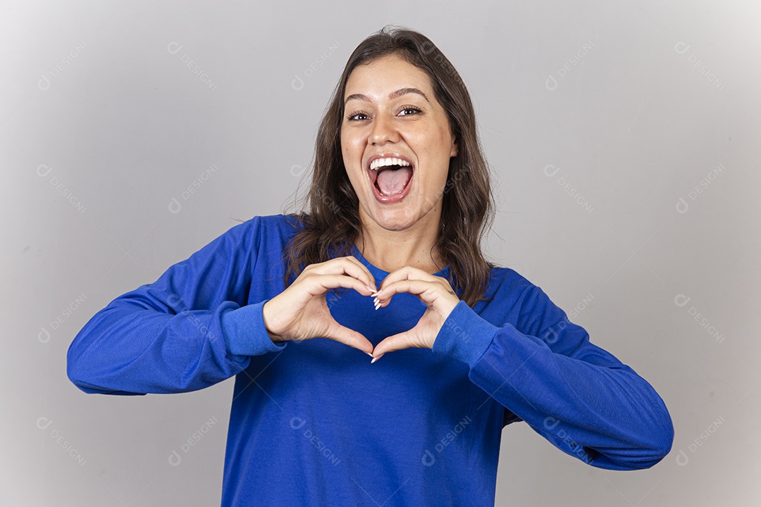 Linda jovem mulher vestida com moletom azul fazendo sinal do coração com as mãos.