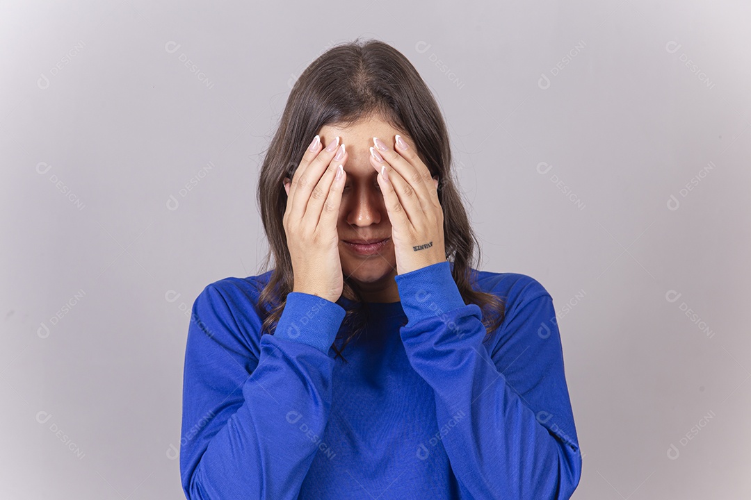 Jovem mulher vestida com moletom azul com as mãos no rosto.