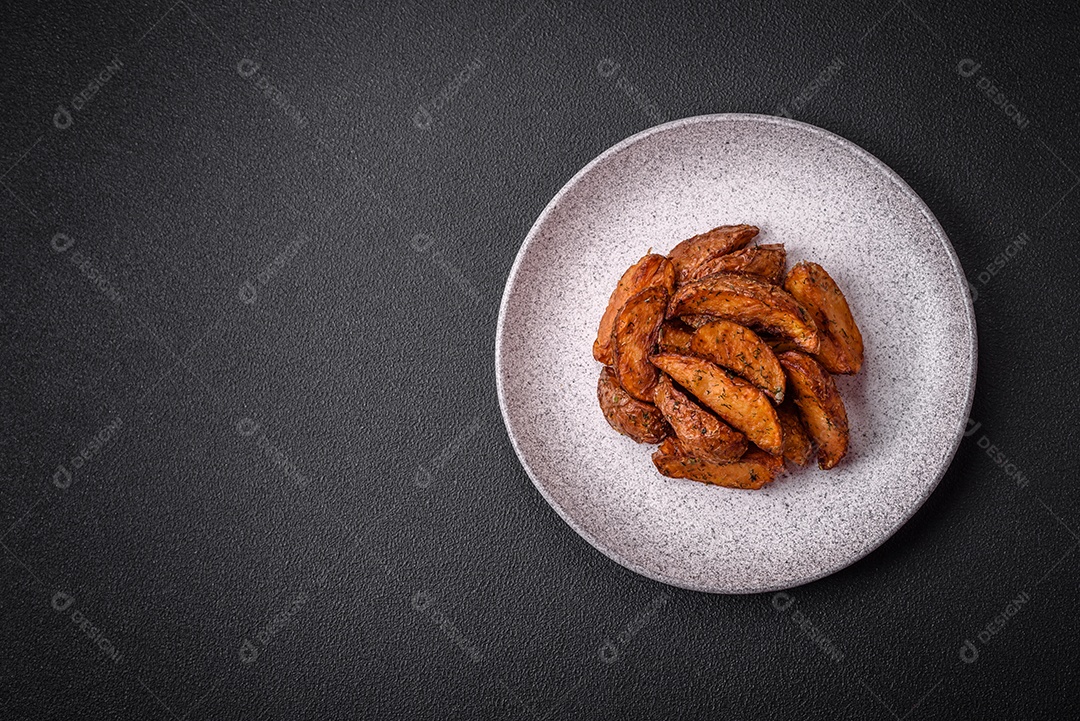 Deliciosas fatias de batata crocante com alho, sal, especiarias e ervas sobre um fundo escuro de concreto