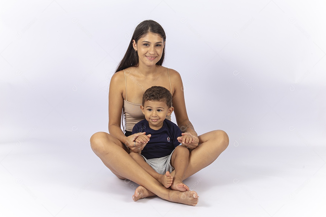 Mãe sentada no chão de frente para o filho sobre um fundo branco.