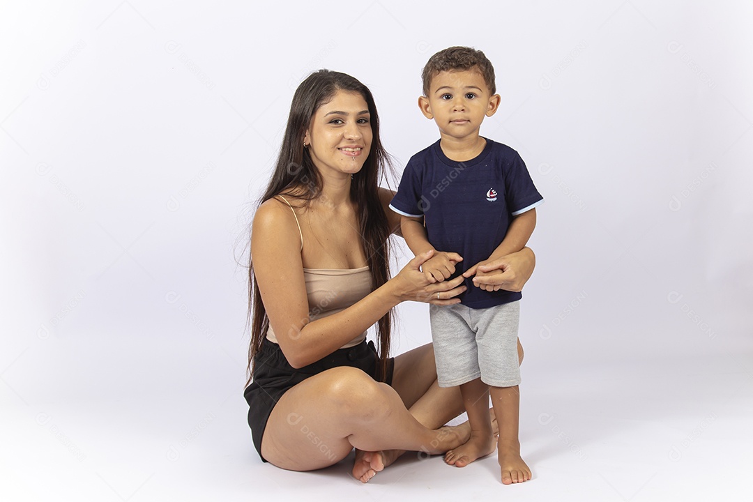 Mãe sentada no chão com filho no colo sobre um fundo branco.