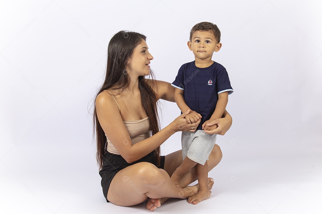 Mãe sentada no chão com filho no colo sobre um fundo branco.