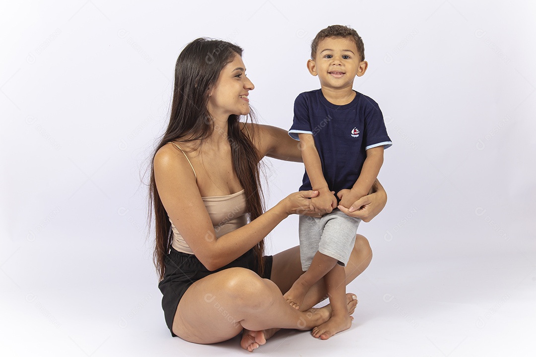 Mãe sentada no chão com filho no colo sobre um fundo branco.