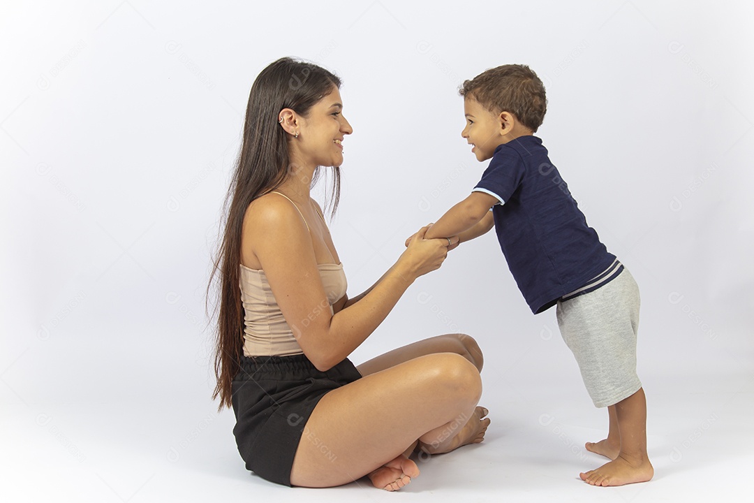 Mãe sentada no chão de frente para o filho sobre um fundo branco.
