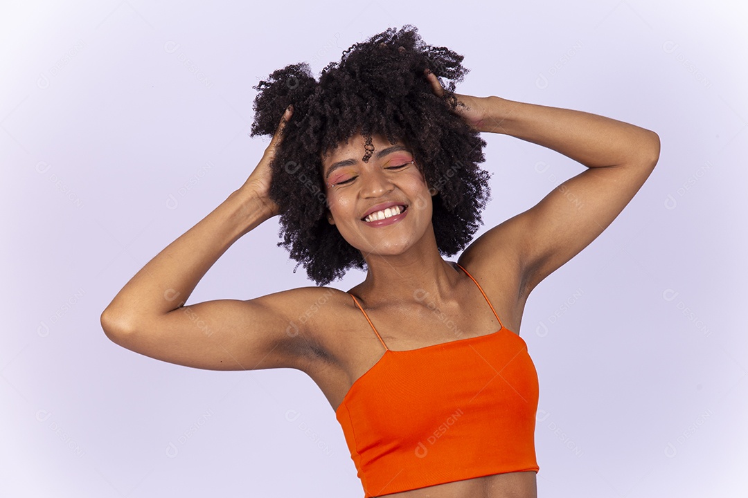 Linda jovem negra com as mão no cabelo usando blusa laranja sobre fundo branco.