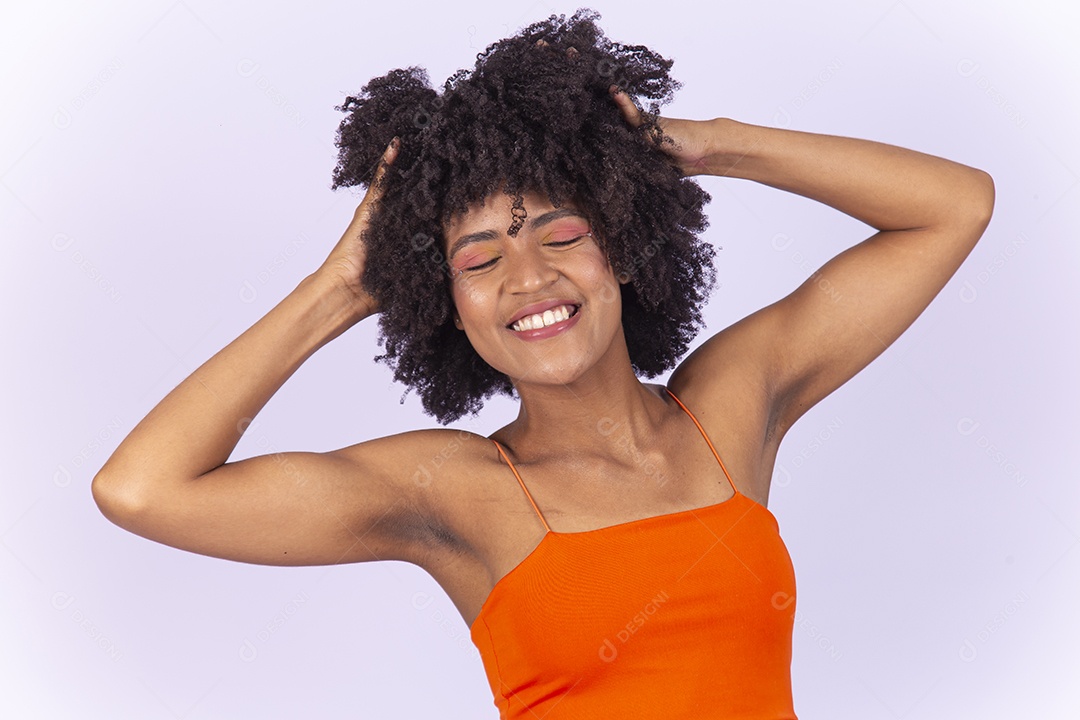 Linda jovem negra com as mão no cabelo usando blusa laranja sobre fundo branco.
