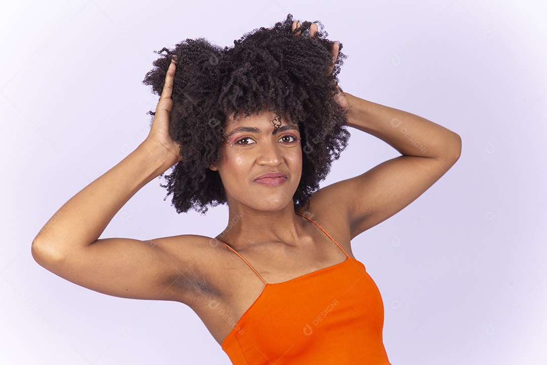 Linda jovem negra com as mão no cabelo usando blusa laranja sobre fundo branco.