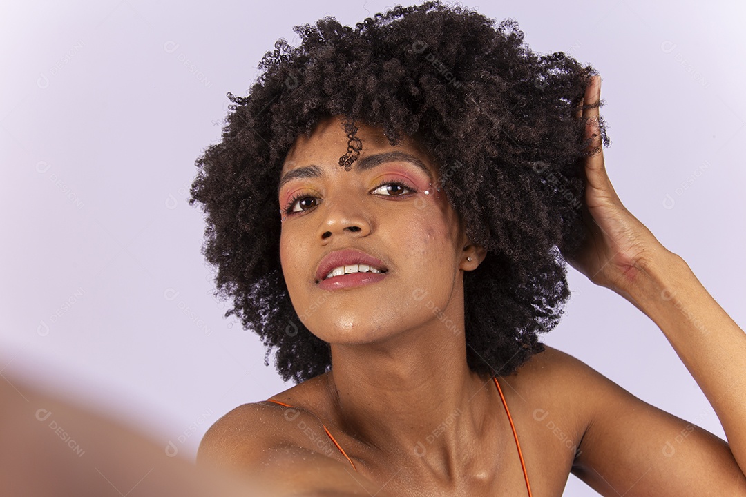 Linda jovem negra de blusa laranja com a mão no cabelo.