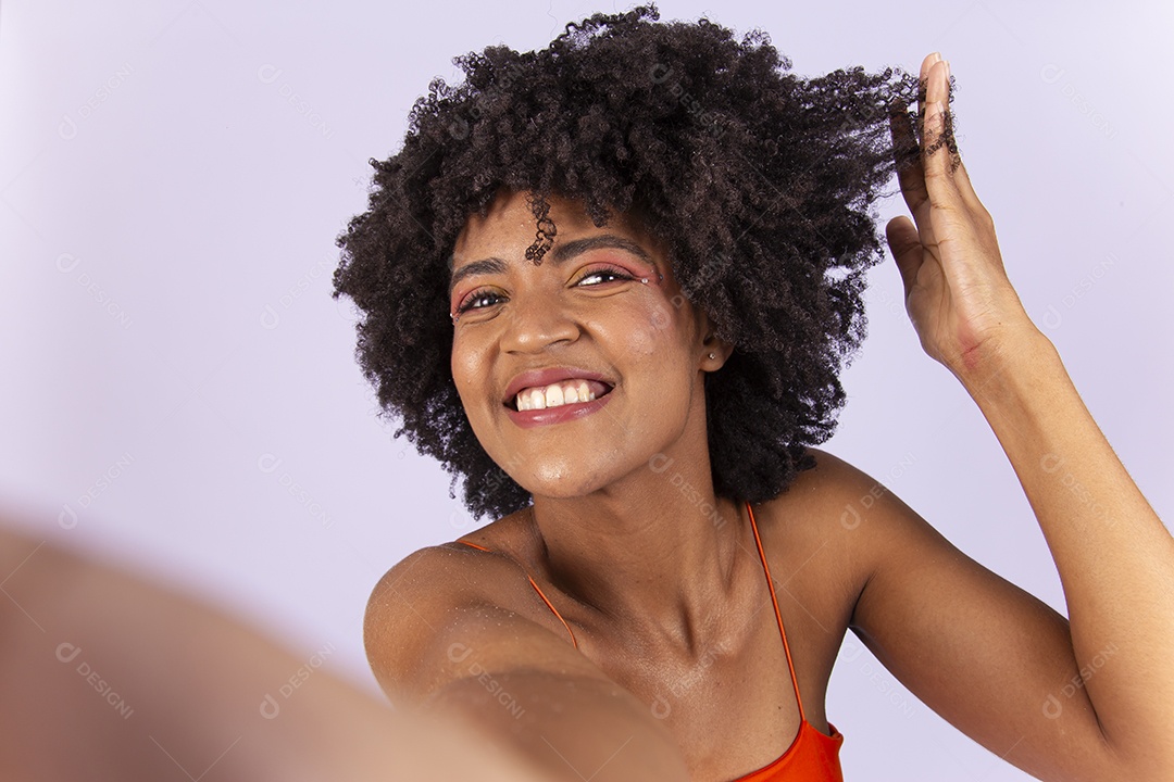 Linda jovem negra de blusa laranja com a mão no cabelo.