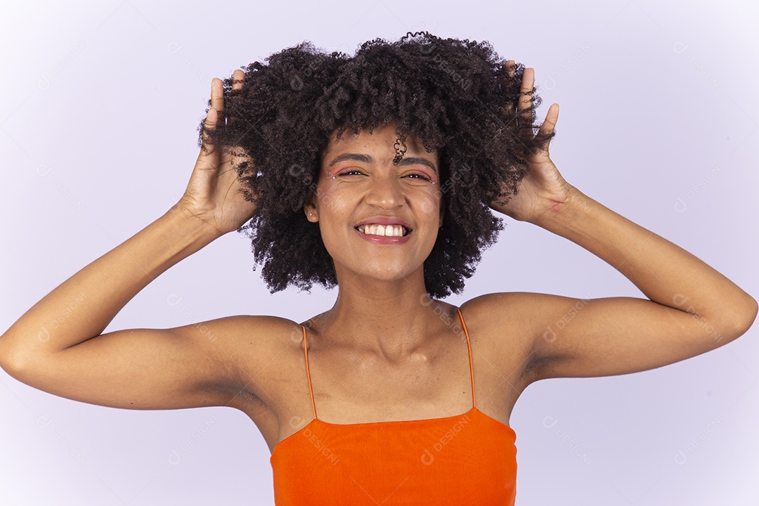 Linda jovem negra de blusa laranja com as mãos no cabelo.