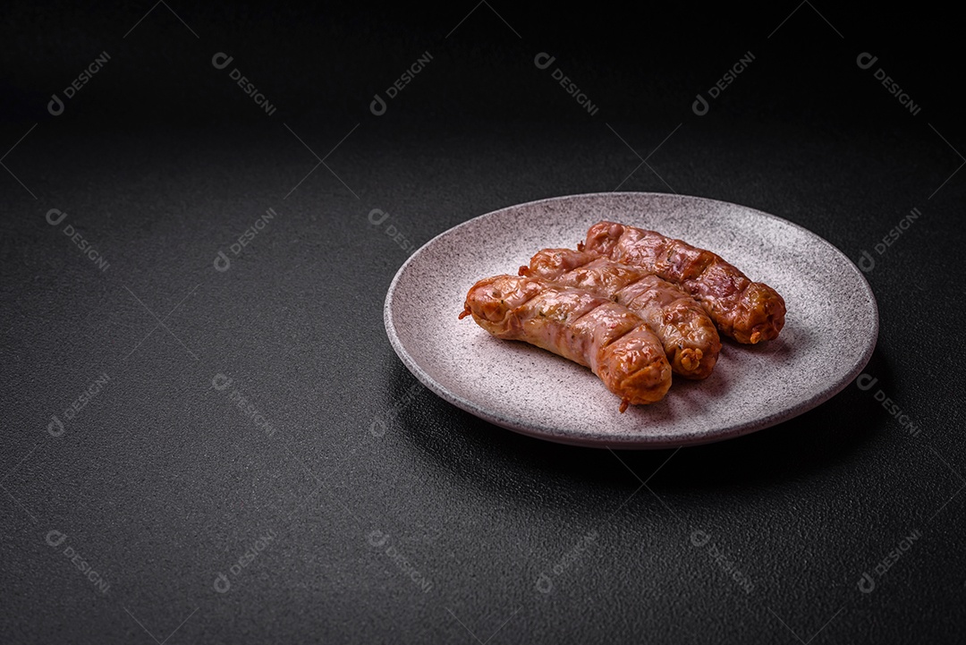 Deliciosos e suculentos enchidos de frango ou porco grelhados com sal, especiarias e ervas sobre um fundo escuro de concreto