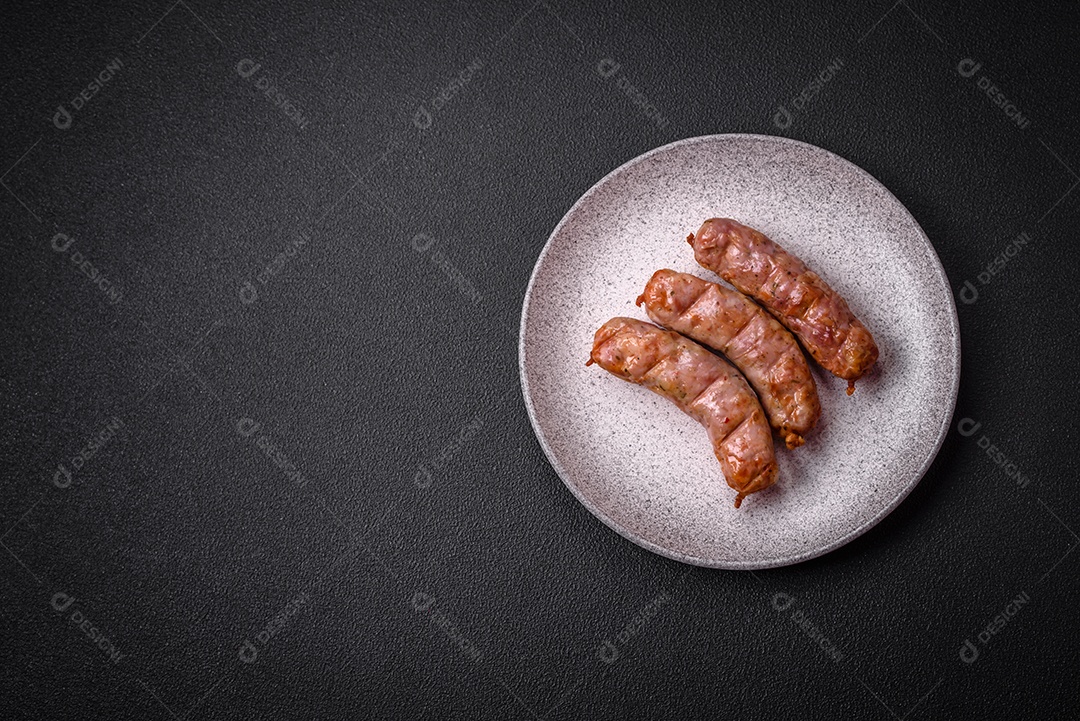 Deliciosos e suculentos enchidos de frango ou porco grelhados com sal, especiarias e ervas sobre um fundo escuro de concreto