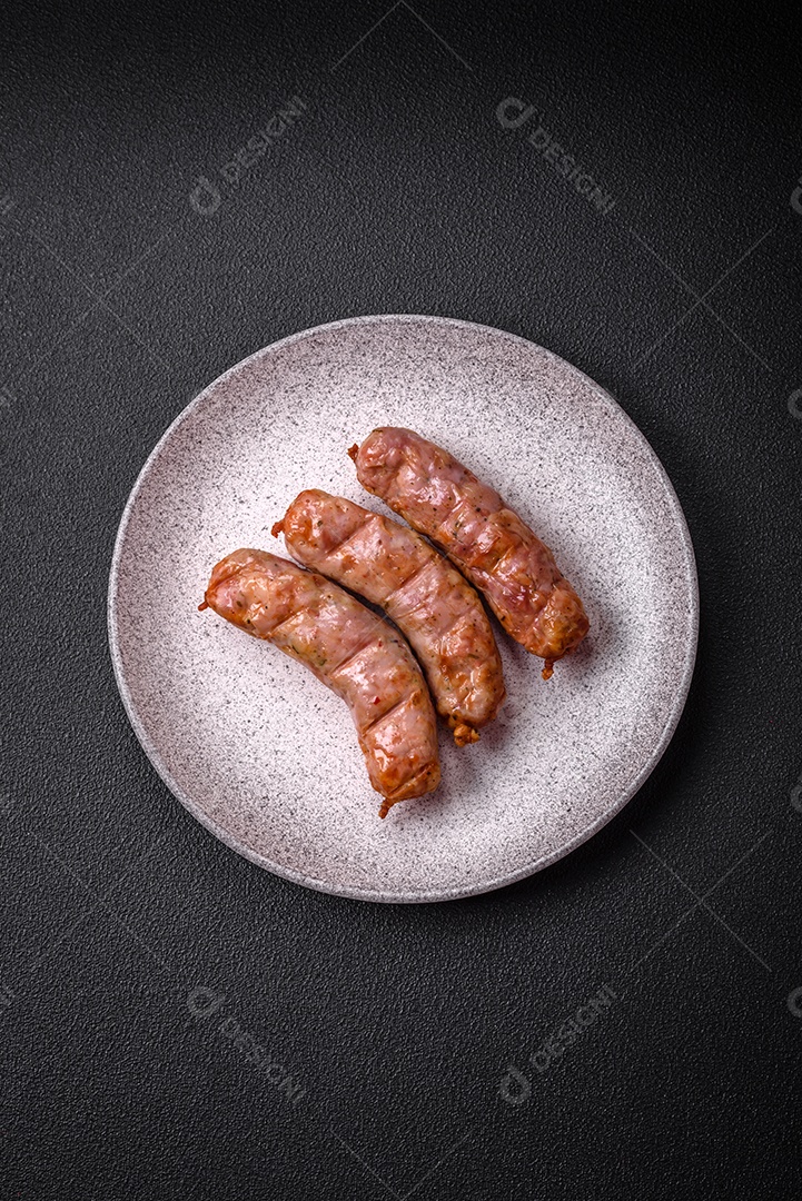 Deliciosos e suculentos enchidos de frango ou porco grelhados com sal, especiarias e ervas sobre um fundo escuro de concreto