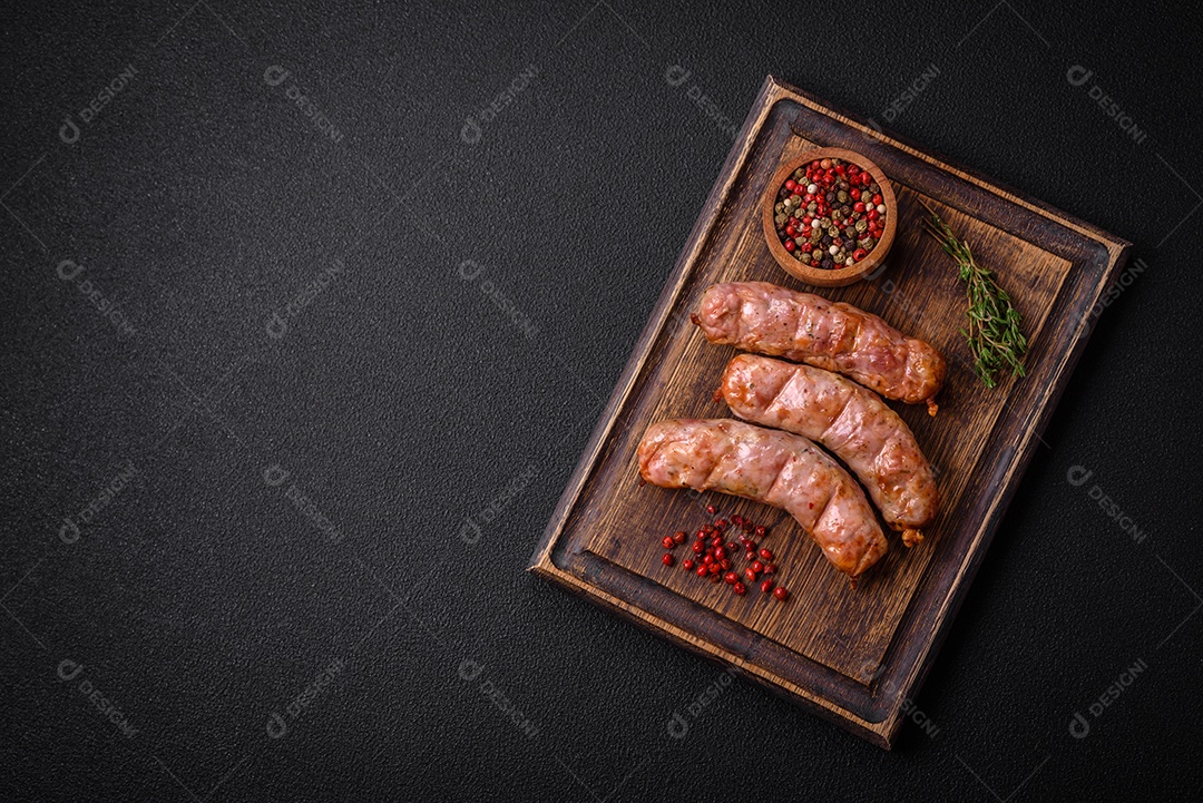 Deliciosos e suculentos enchidos de frango ou porco grelhados com sal, especiarias e ervas sobre um fundo escuro de concreto