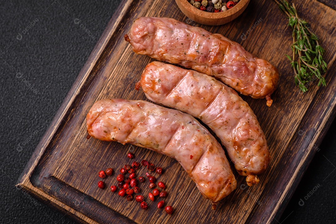 Deliciosos e suculentos enchidos de frango ou porco grelhados com sal, especiarias e ervas sobre um fundo escuro de concreto