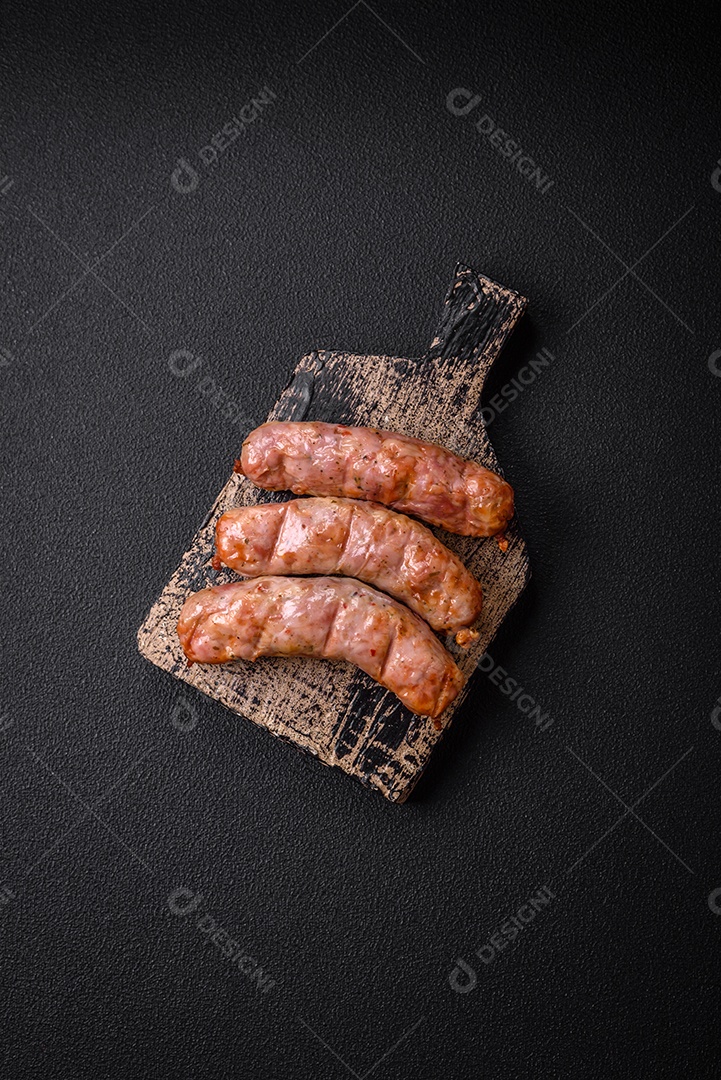 Deliciosos e suculentos enchidos de frango ou porco grelhados com sal, especiarias e ervas sobre um fundo escuro de concreto