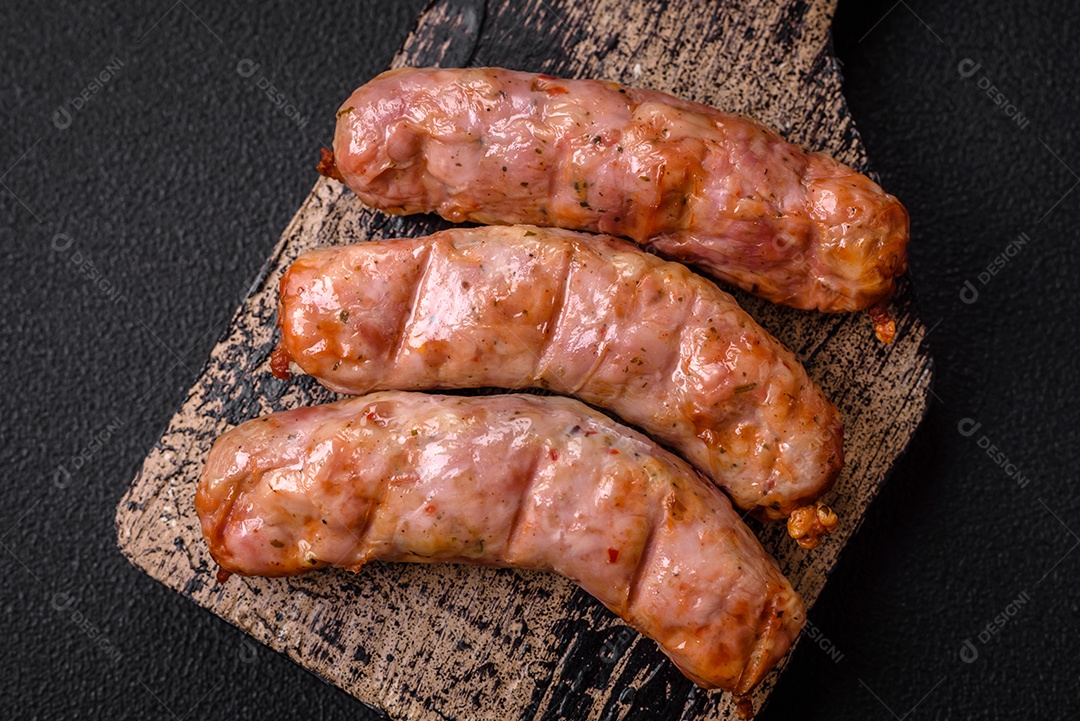 Deliciosos e suculentos enchidos de frango ou porco grelhados com sal, especiarias e ervas sobre um fundo escuro de concreto