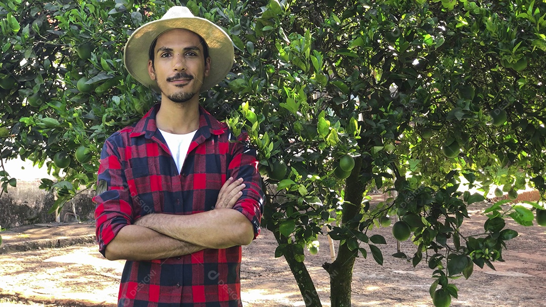 Agricultor com chapéu olhando para a câmera em frente a uma laranjeira