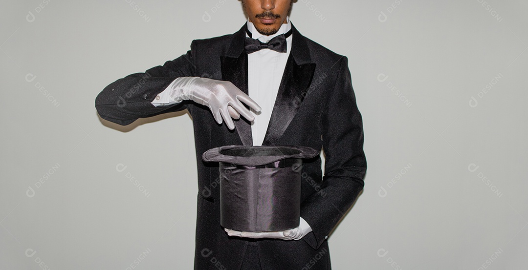 Jovem mágico ilusionista negro fazendo mágica com uma cartola e uma varinha mágica