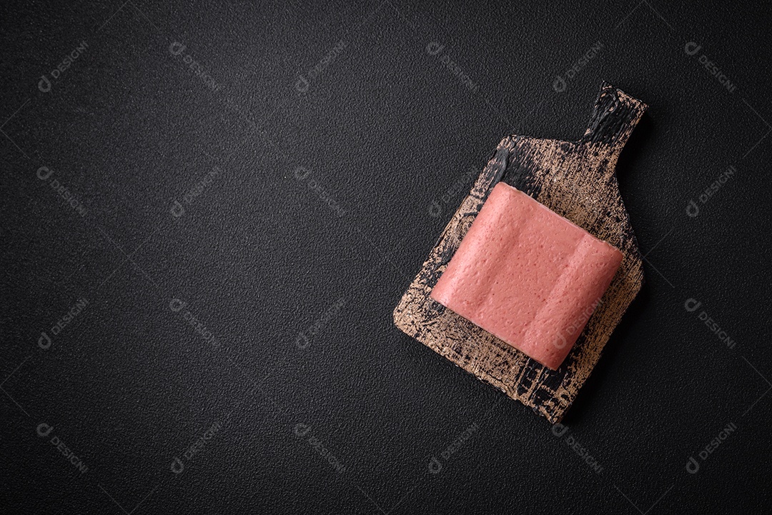 Delicioso presunto rosa enlatado com sal, especiarias e ervas sobre um fundo escuro de concreto