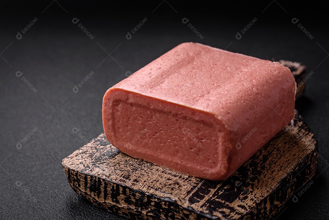 Delicioso presunto rosa enlatado com sal, especiarias e ervas sobre um fundo escuro de concreto