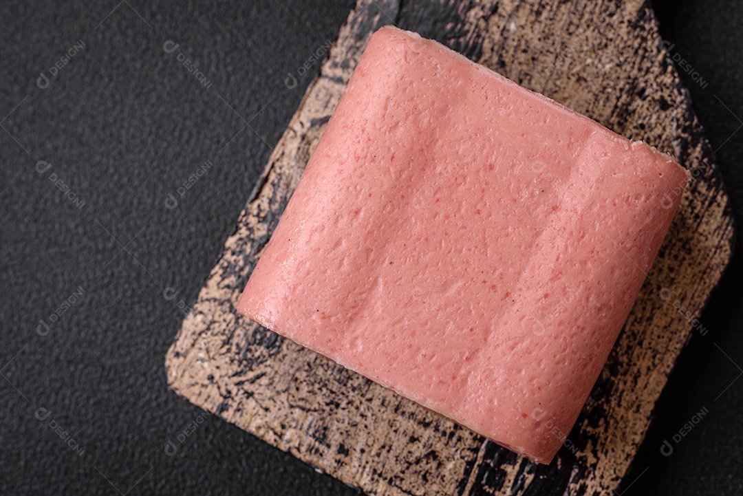 Delicioso presunto rosa enlatado com sal, especiarias e ervas sobre um fundo escuro de concreto