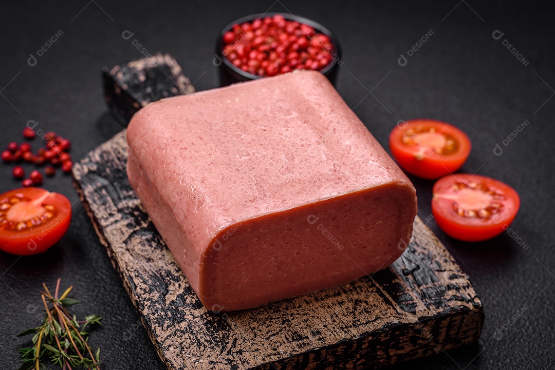 Delicioso presunto rosa enlatado com sal, especiarias e ervas sobre um fundo escuro de concreto