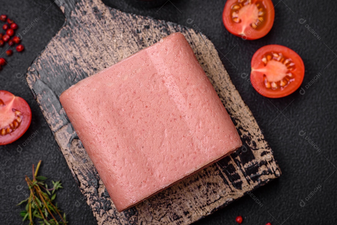 Delicioso presunto rosa enlatado com sal, especiarias e ervas sobre um fundo escuro de concreto