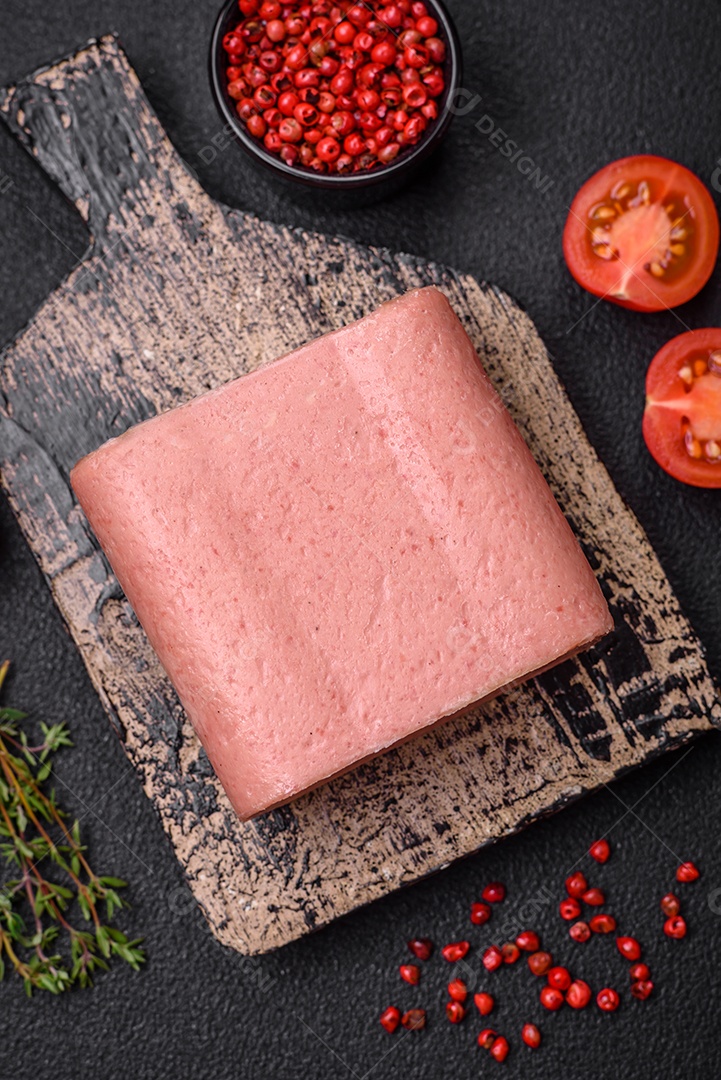 Delicioso presunto rosa enlatado com sal, especiarias e ervas sobre um fundo escuro de concreto