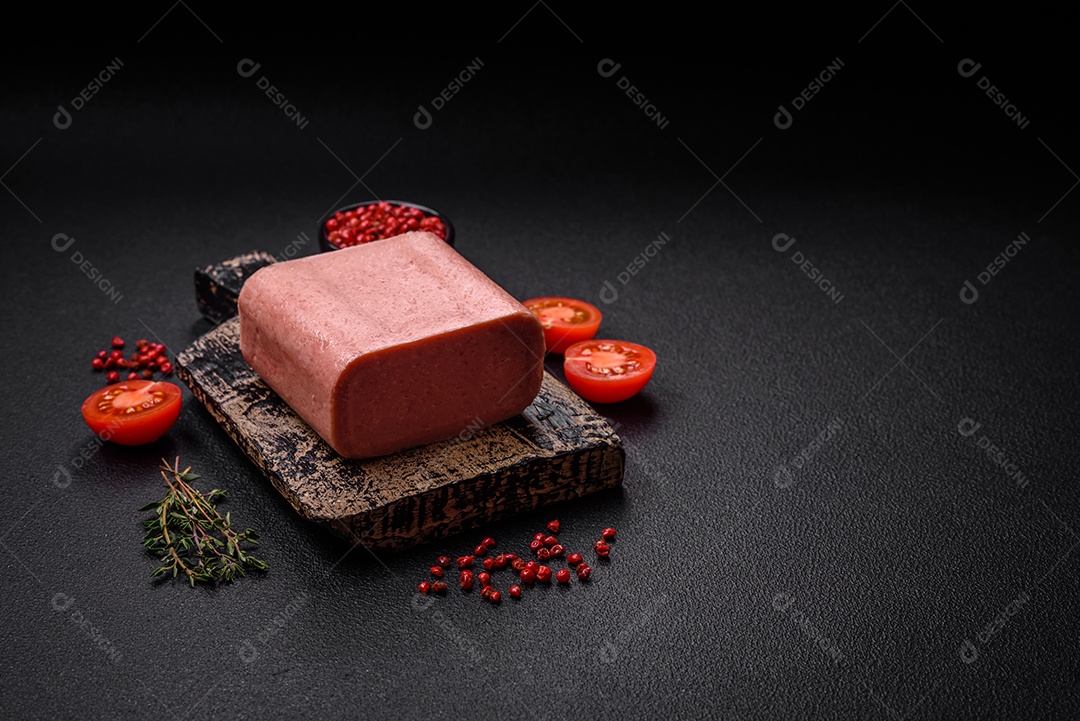 Delicioso presunto rosa enlatado com sal, especiarias e ervas sobre um fundo escuro de concreto