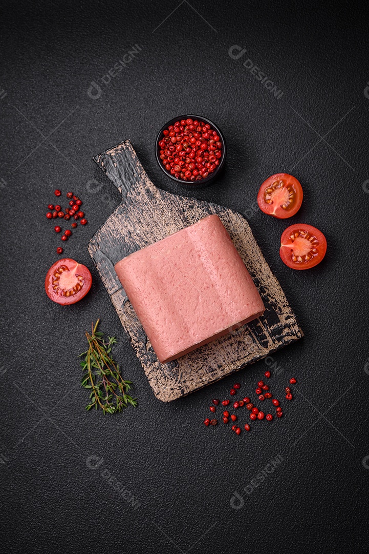 Delicioso presunto rosa enlatado com sal, especiarias e ervas sobre um fundo escuro de concreto