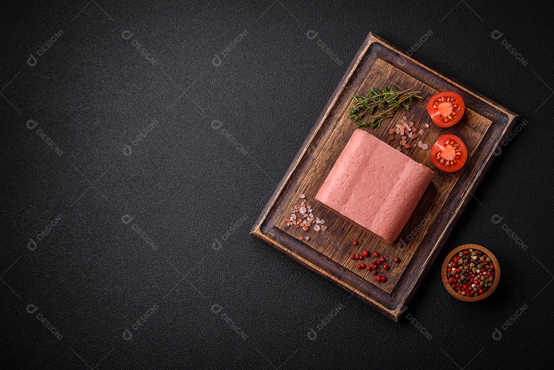 Delicioso presunto rosa enlatado com sal, especiarias e ervas sobre um fundo escuro de concreto