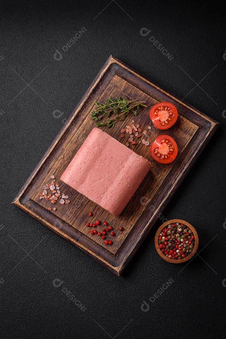 Delicioso presunto rosa enlatado com sal, especiarias e ervas sobre um fundo escuro de concreto