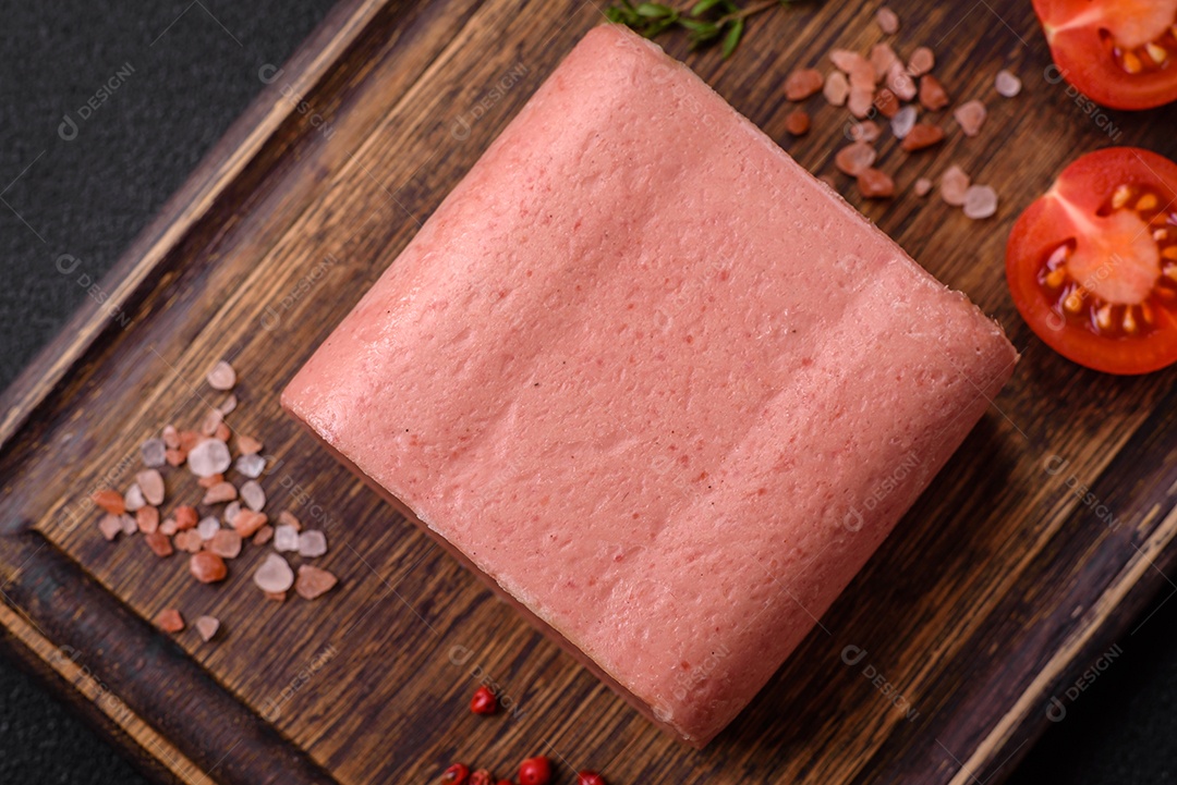 Delicioso presunto rosa enlatado com sal, especiarias e ervas sobre um fundo escuro de concreto
