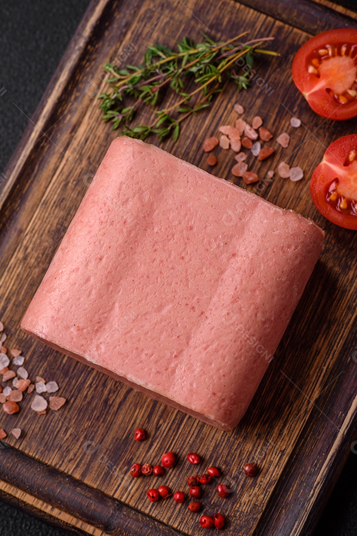 Delicioso presunto rosa enlatado com sal, especiarias e ervas sobre um fundo escuro de concreto