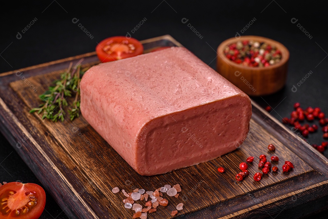 Delicioso presunto rosa enlatado com sal, especiarias e ervas sobre um fundo escuro de concreto