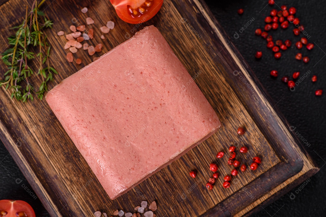 Delicioso presunto rosa enlatado com sal, especiarias e ervas sobre um fundo escuro de concreto