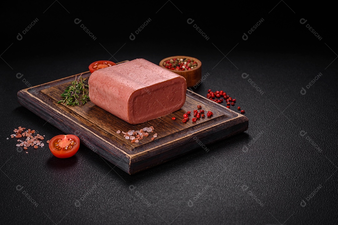 Delicioso presunto rosa enlatado com sal, especiarias e ervas sobre um fundo escuro de concreto