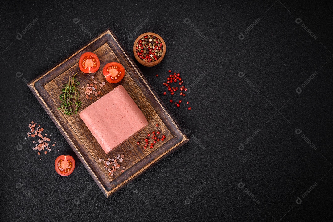 Delicioso presunto rosa enlatado com sal, especiarias e ervas sobre um fundo escuro de concreto