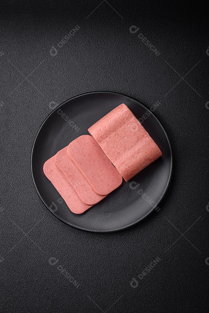Delicioso presunto rosa enlatado com sal, especiarias e ervas sobre um fundo escuro de concreto