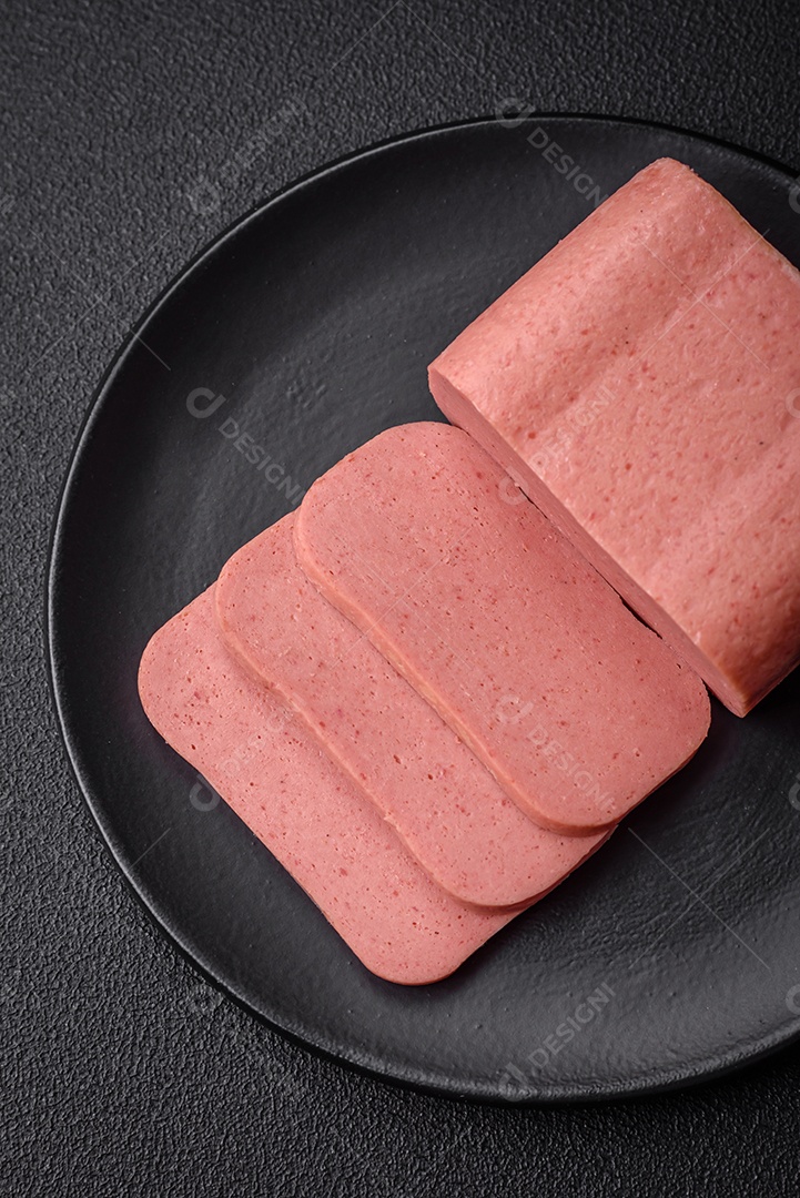Delicioso presunto rosa enlatado com sal, especiarias e ervas sobre um fundo escuro de concreto