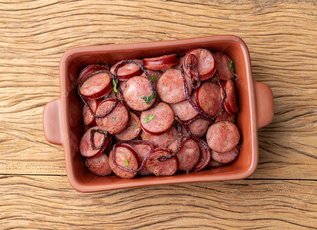 Porção de calabresa com cebola sobre fundo de madeira