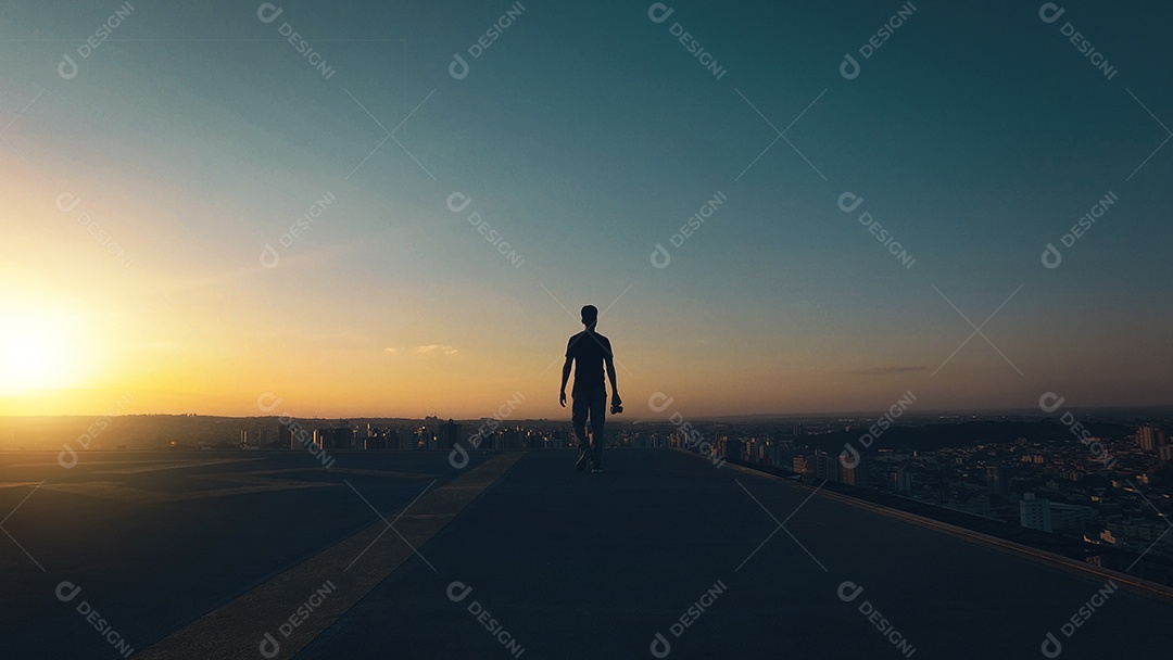 Silhueta de um homem caminhando no topo do prédio ao pôr do sol e céu nublado