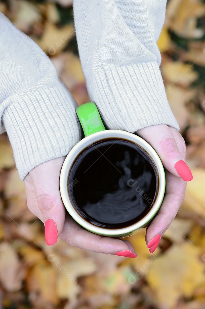 Mão feminina segurando uma xícara de café sobre fundo de folhagem do outono